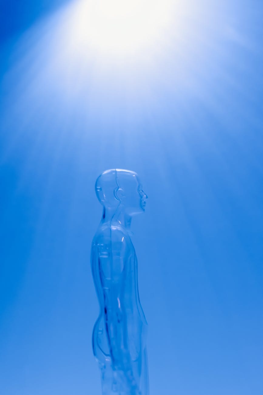 Transparent plastic human figure in profile view against a blue background, symbolizing technology, innovation, and the blending of humans with artificial intelligence.