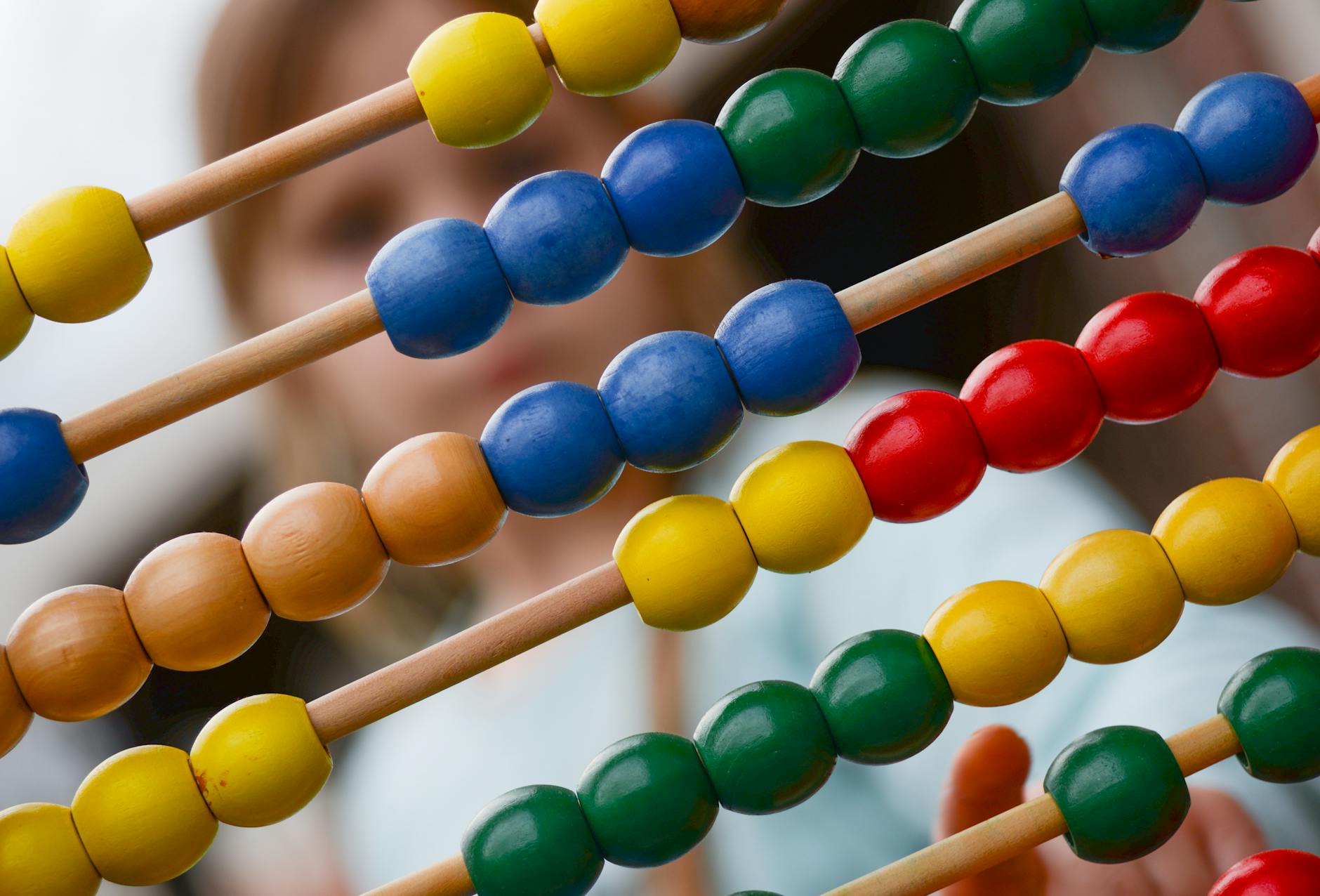 Close-up of a colorful abacus with a child in soft focus behind it, hand raised to count, symbolizing early math and hands-on learning.