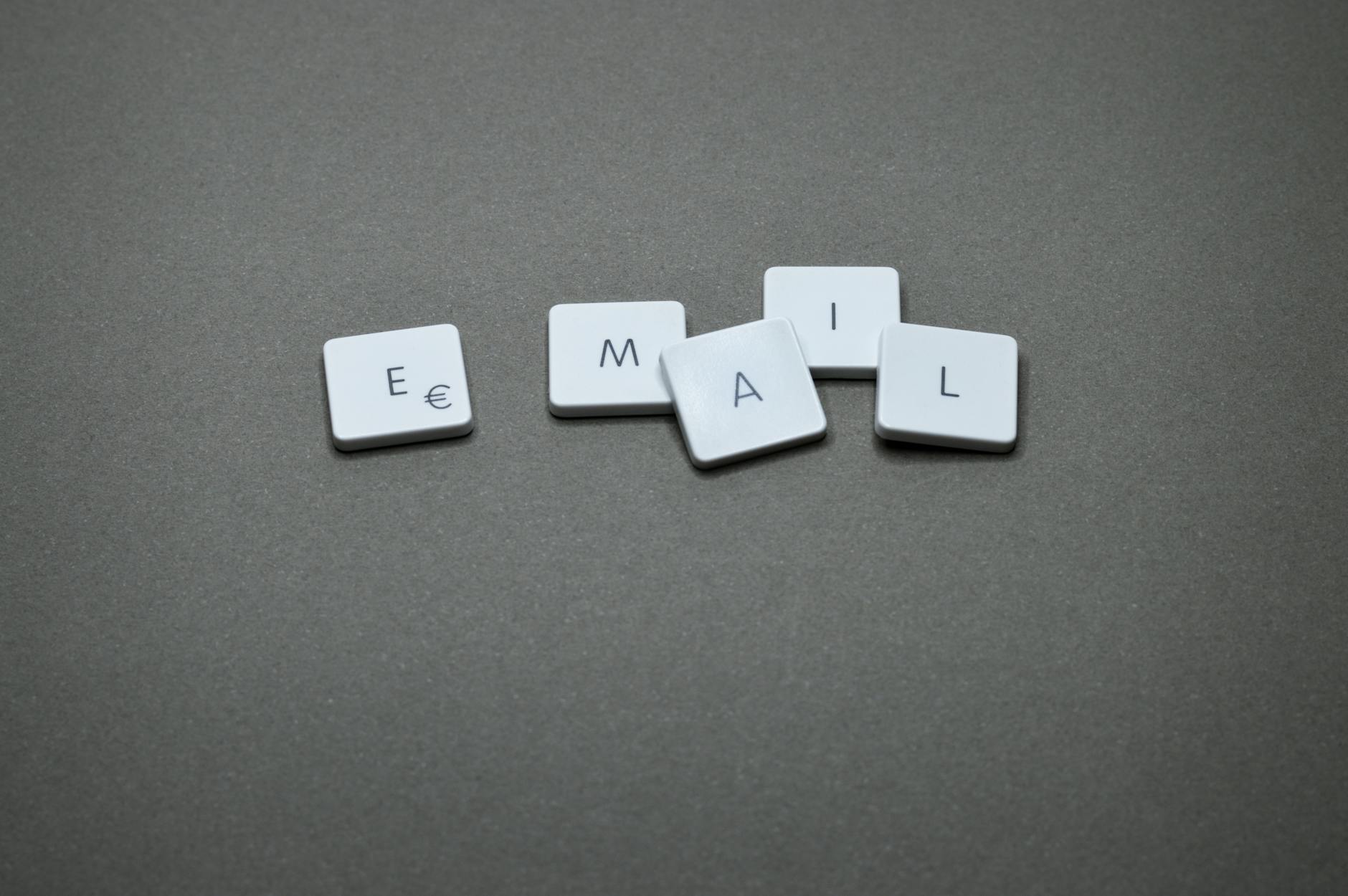 email bl“EMAIL” spelled with white tiles on a gray background, illustrating AI email marketing basics.ocks on gray surface