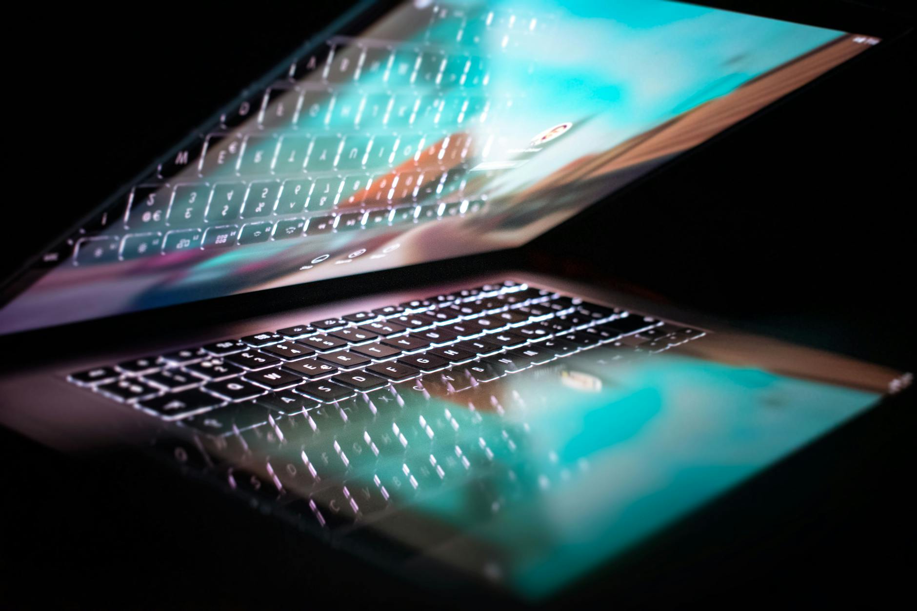 A close-up of a laptop partially closed, reflecting its illuminated keyboard on the screen, symbolizing technology, innovation, and digital connection in a modern workspace.