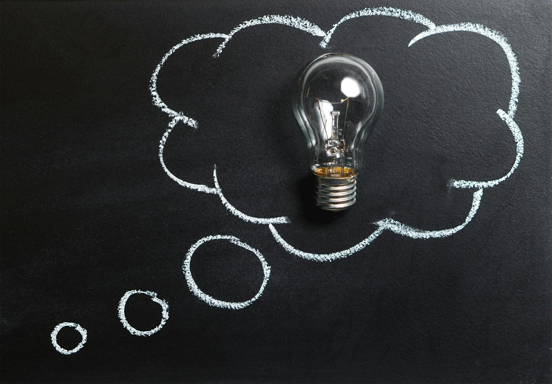 A light bulb rests inside a chalk-drawn thought bubble on a blackboard, representing creative thinking, brainstorming, and the spark of new ideas.