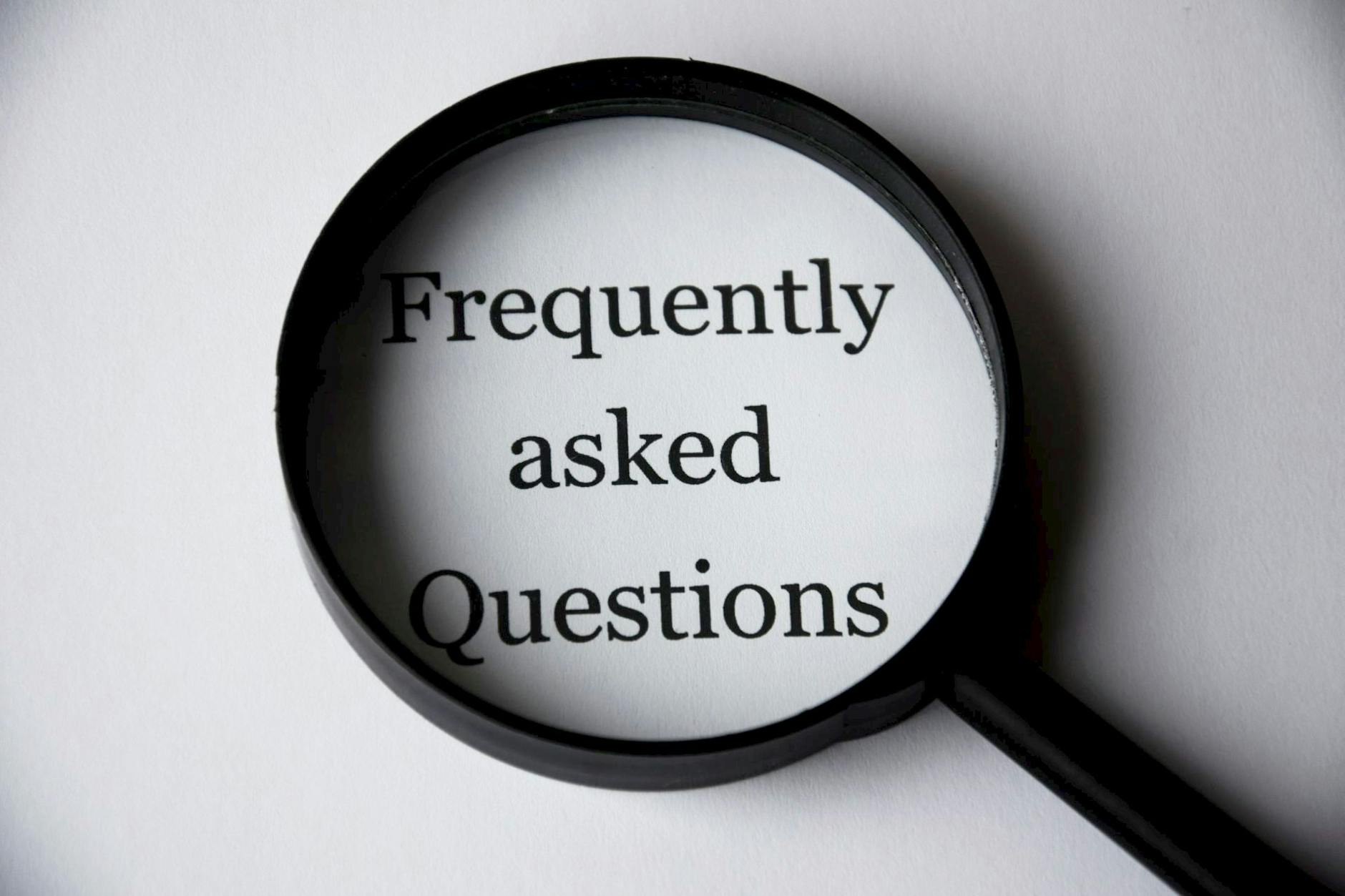 Magnifying glass highlighting the words ‘Frequently Asked Questions’ on a white background.